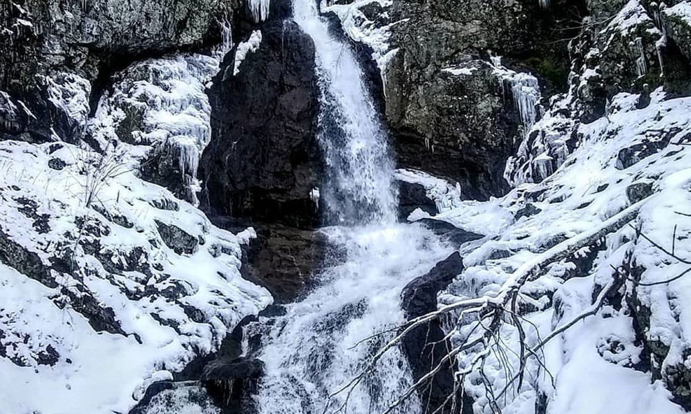 A waterfall travels through a snowy landscape