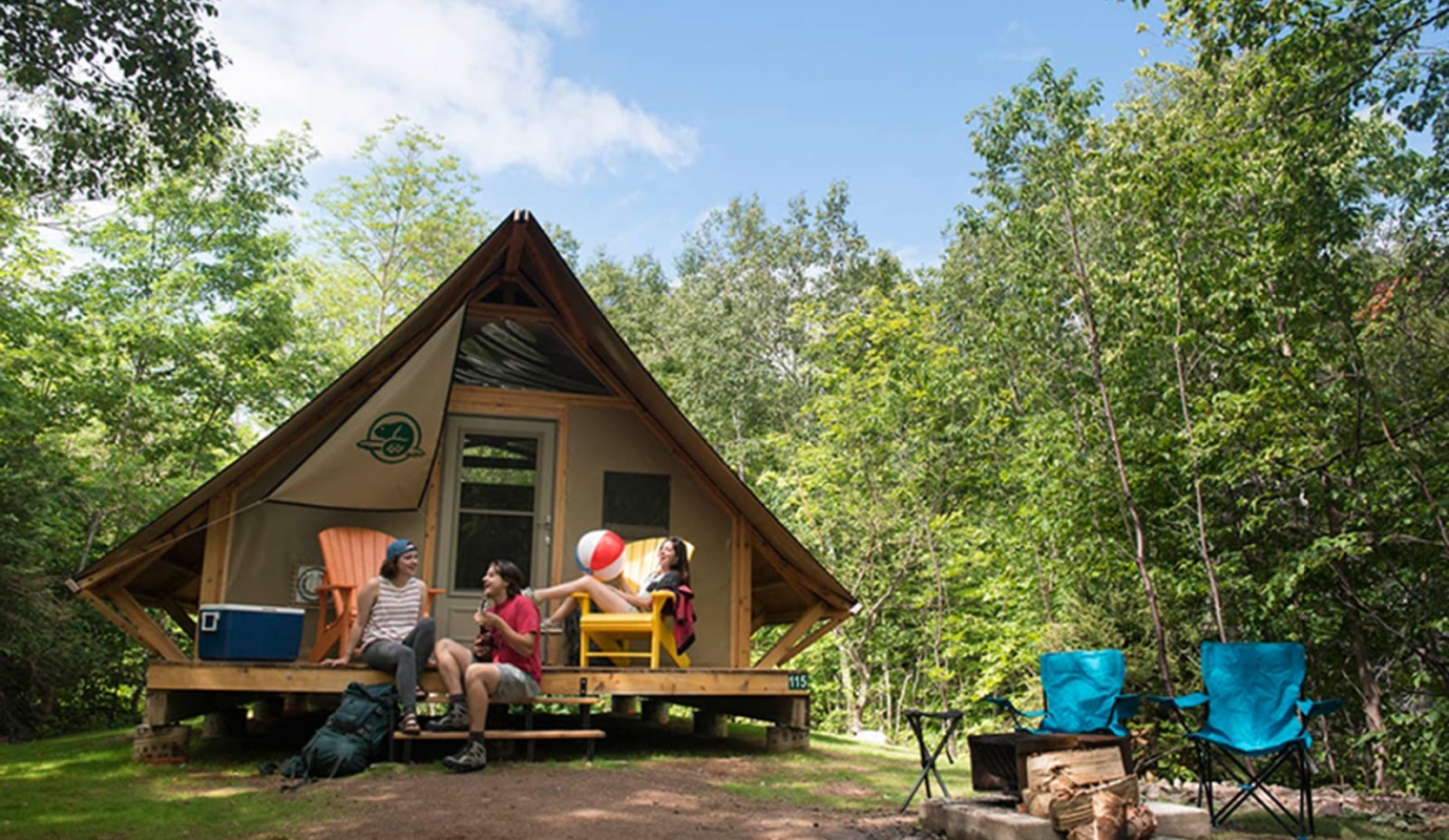 Three young girls sit outside an a-frame tent in the woods