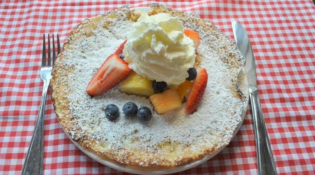 A pie dusted with icing sugar, fresh fruit, and whipped cream