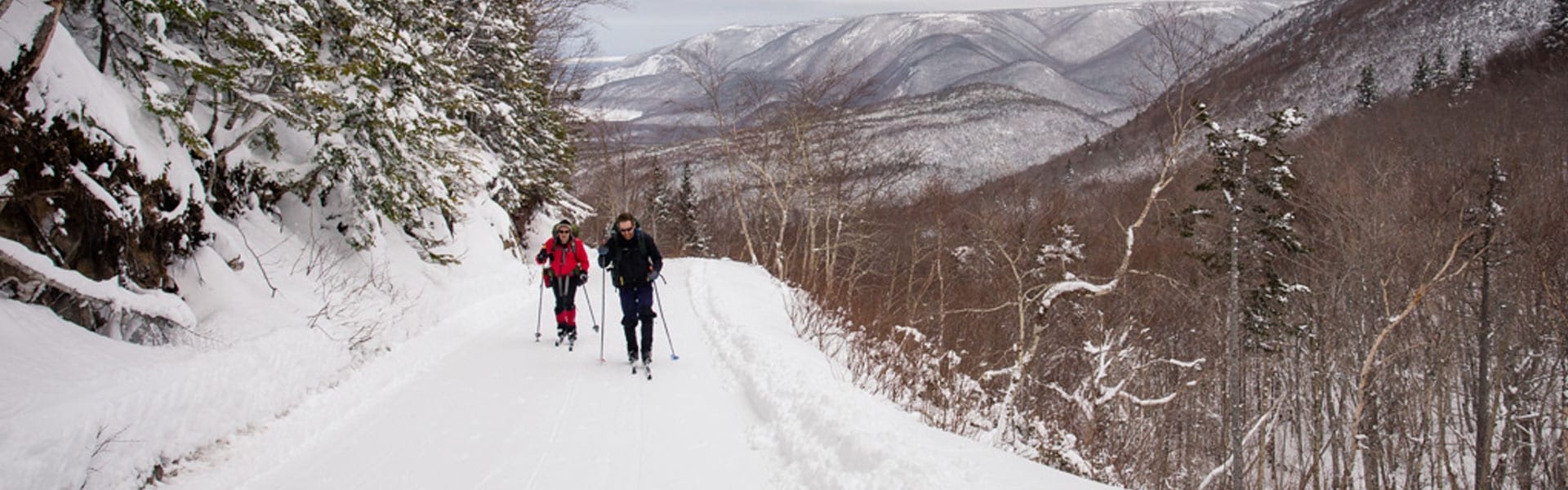 A couple cross country ski with snowy mountains in the background