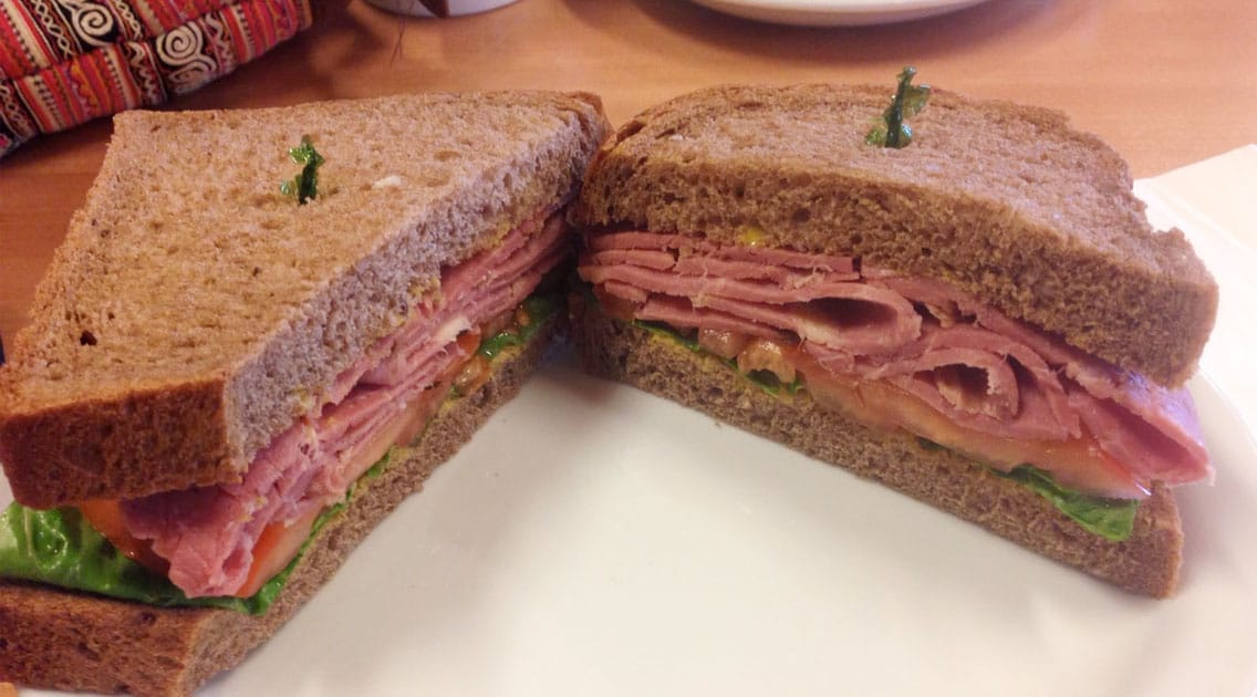 A pastrami, lettuce, and tomato sandwich on whole wheat bread