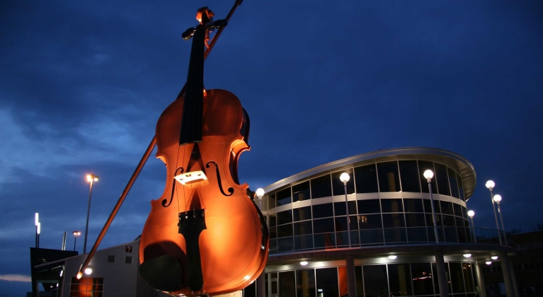 An art installation of a large violin statue in front of a theatre