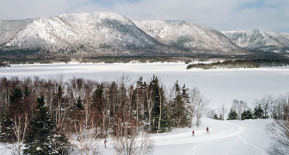 Cross country skiers travel a path that overlook the ocean and the mountains