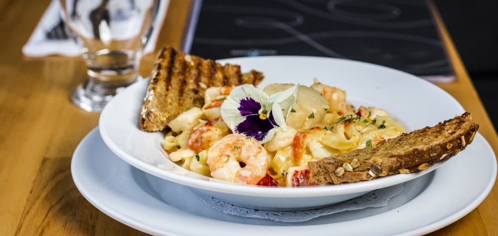 A dish of seafood linguine with bread and an edible flower