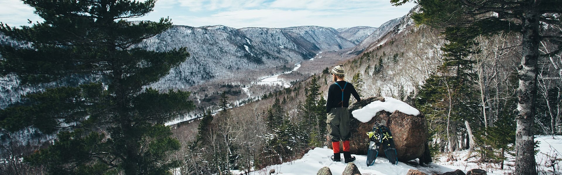 A man and his snowshoes stand next to a rock overlooking a snowy landscape