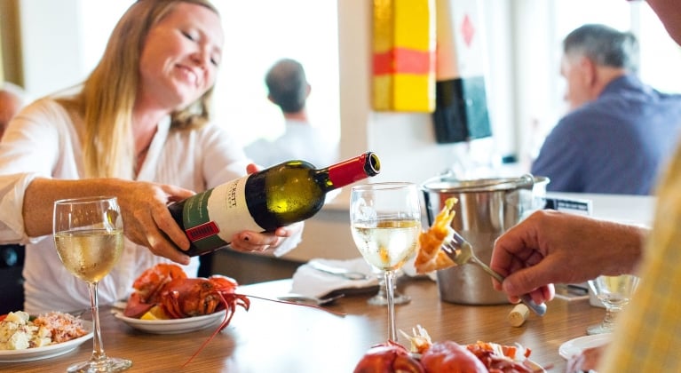 A woman tops up a glass of wine at a lobster dinner