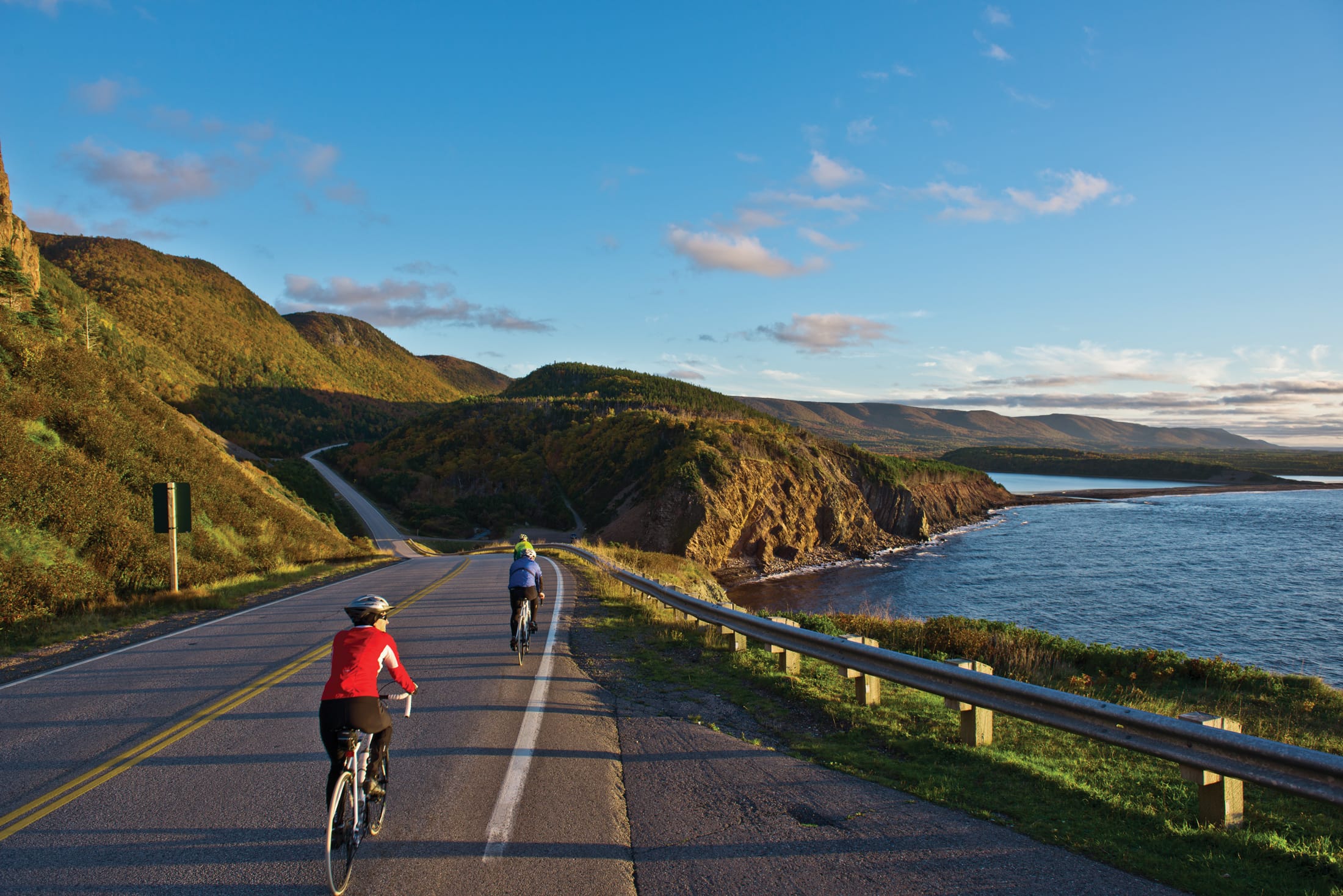 Bikers pedal down the highway overlooking the ocean