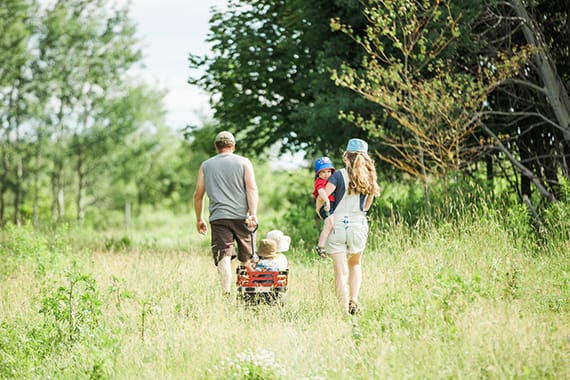 A family walks through a grassy field, pulling the children in a wagon