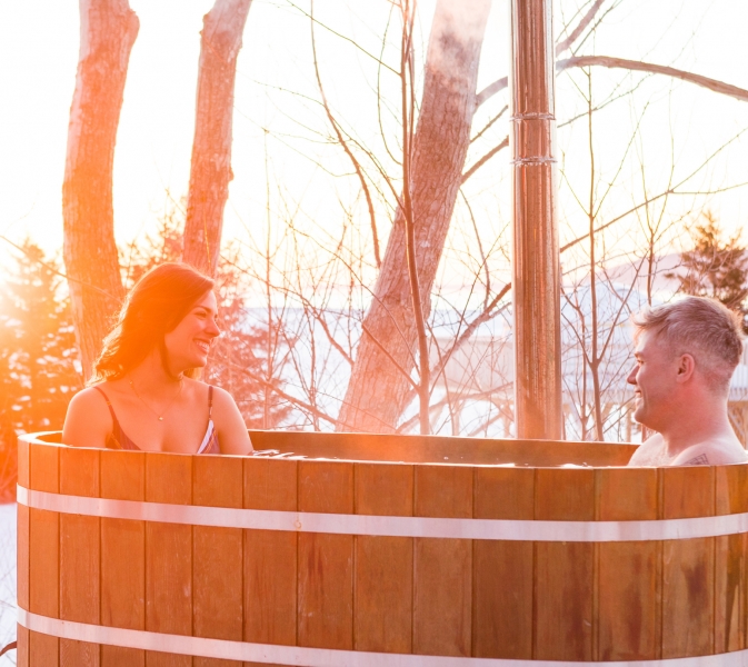 couple sit in outdoor wooden hot tub in winter