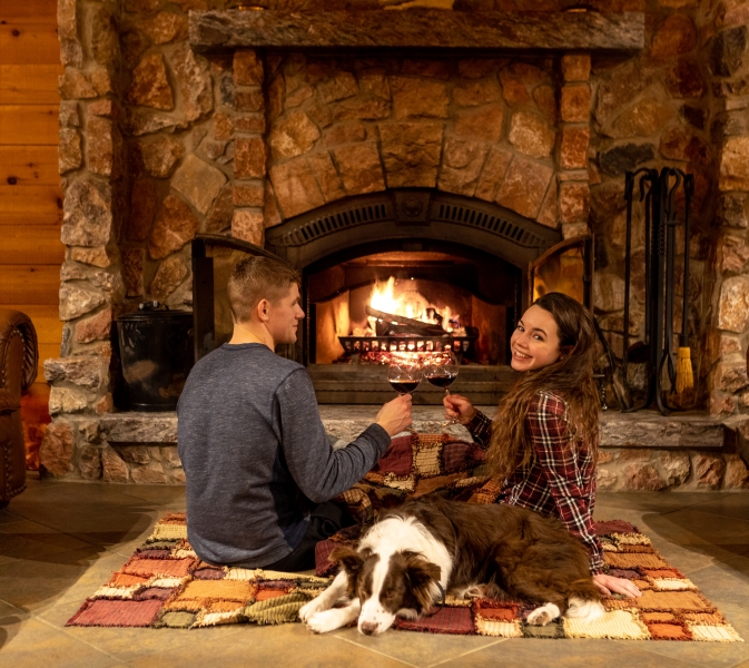 a couple and their dog sit on a run in front of a fire