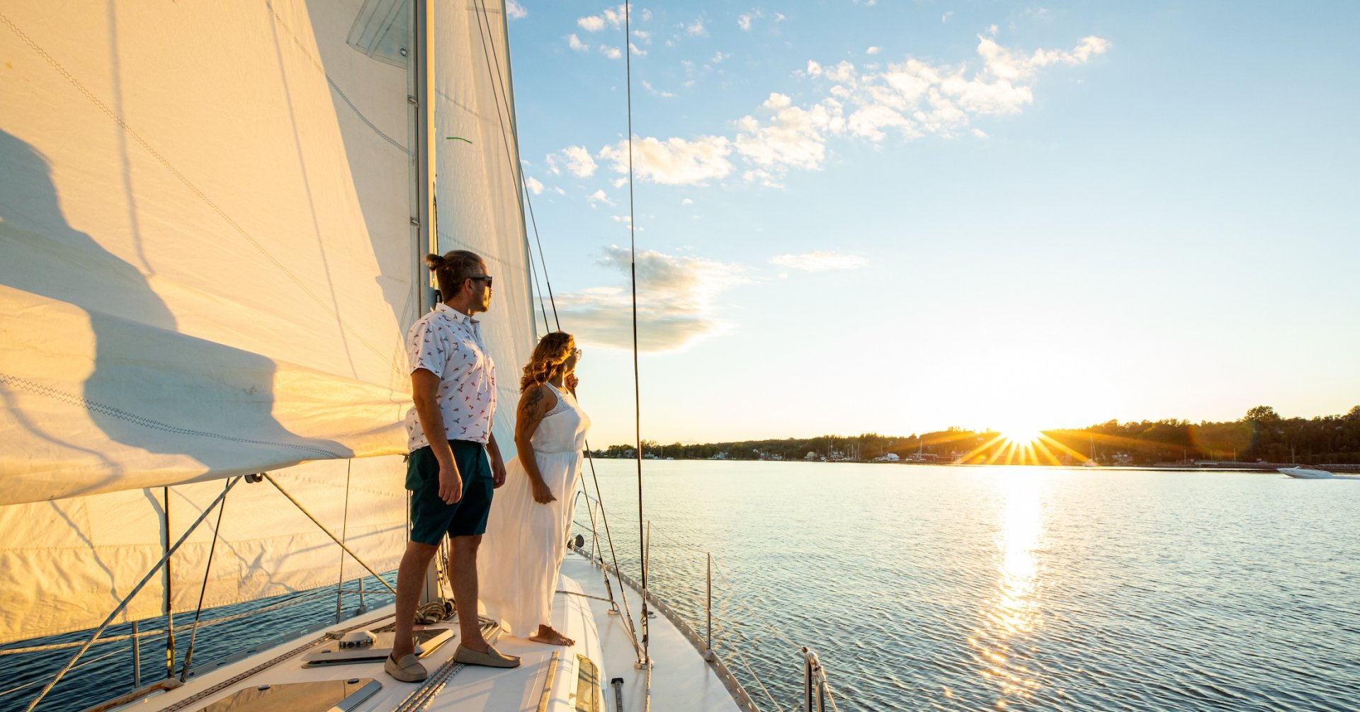 a couple stands on a sailboat looking at the setting sun